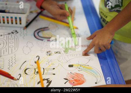 Un bambino siede e colora un gigantesco motivo di carta da colorare. Il bambino tiene in mano una matita. Un set di matite colorate su una scatola. Attività di disegno. Foto Stock