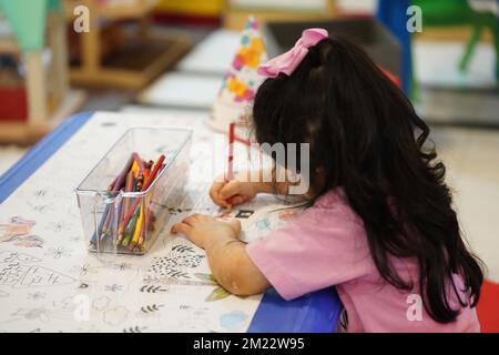 Un bambino siede e colora un gigantesco motivo di carta da colorare. Il bambino tiene in mano una matita. Un set di matite colorate su una scatola. Attività di disegno. Foto Stock