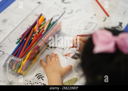 Un bambino siede e colora un gigantesco motivo di carta da colorare. Il bambino tiene in mano una matita. Un set di matite colorate su una scatola. Attività di disegno. Foto Stock