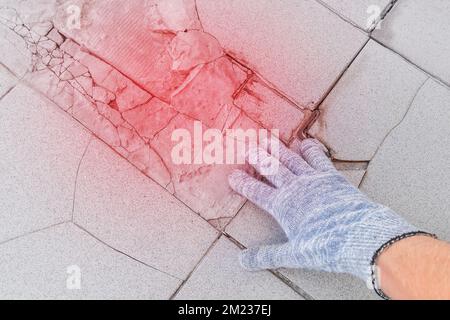 Mano di lavoro di costruzione maschile in guanti protettivi esamina vecchio pavimento di piastrelle rotto sfondo. Concetto di rinnovamento. Foto Stock
