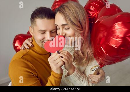 Ritratto di adorabile coppia carina innamorata che con gli occhi chiusi tiene insieme il cuore di carta rossa. Foto Stock