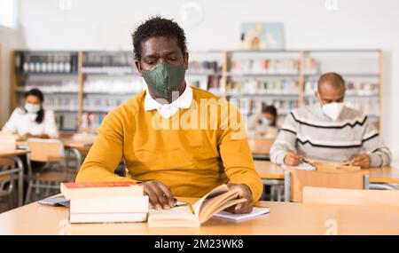 Afroamericano adulto in maschera protettiva visitando la biblioteca pubblica Foto Stock