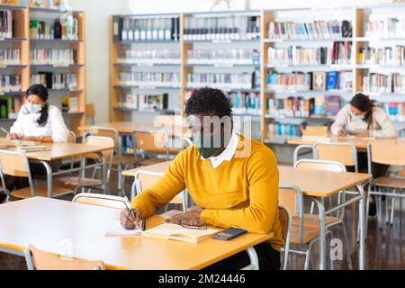Afroamericano adulto in maschera protettiva visitando la biblioteca pubblica Foto Stock