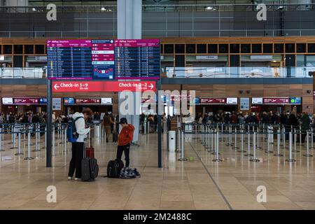 BERLINO, GERMANIA - 12 DICEMBRE 2022: Gli orari di partenza sono riportati sugli schermi con il passeggero che controlla gli orari dei voli al telefono. Aeroporto BER ancora Foto Stock
