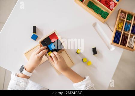 Bambino maschio mani montaggio trinomiale cubo legno Montessori materiale sulla scrivania primo piano vista dall'alto Foto Stock