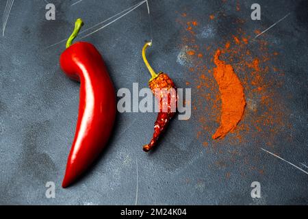 Pepe rosso in varie fasi. Pepe rosso crudo, peperoncino in polvere essiccato e rosso su fondo scuro. Foto Stock