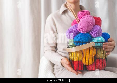 Una giovane donna tiene in braccio un elegante cesto di filo nero. Palle e matasse di filato colorato. Foto Stock