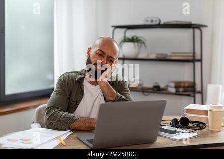 Triste uomo latino sovraccarico seduto alla scrivania di fronte al computer portatile in ufficio a casa e guardando lo schermo, spazio libero Foto Stock