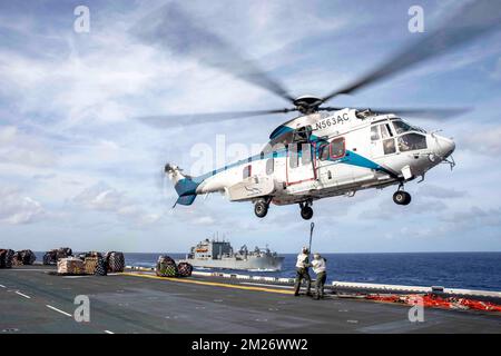 Mar Cinese Meridionale. 4th Dec, 2022. NEGLI STATI UNITI L'elicottero Airbus H225 Super Puma si prepara a ritirare le attrezzature per la movimentazione del carico durante un rifornimento in mare sul ponte di volo della nave d'assalto anfibia USS Makin Island (LHD 8). I rifornimenti in mare assicurano che l'equipaggio riceva e mantenga un'adeguata fornitura di cibo, oltre al trasporto di posta e pacchi dalla nave. Il Makin Island Amphibious Ready Group, composto dalla nave d'assalto anfibio USS Makin Island (LHD 8) e dal porto di trasporto anfibio USS Anchorage (LPD 23) e USS John P. Murtha (LPD 26), opera nella U.S. 7th Fleet are Foto Stock