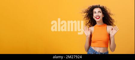 Spensierata e felice urban femminile elegante con naso ad anello e capelli ricci che alzano le palme in un gesto indifferente e indifferente guardando al sole Foto Stock