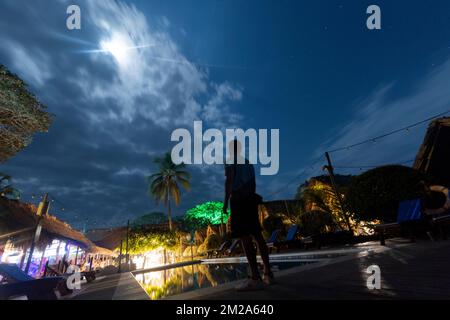 Giovane uomo che guarda in su notte stellata con luna piena alla spiaggia ostea dei caraibi. Foto Stock