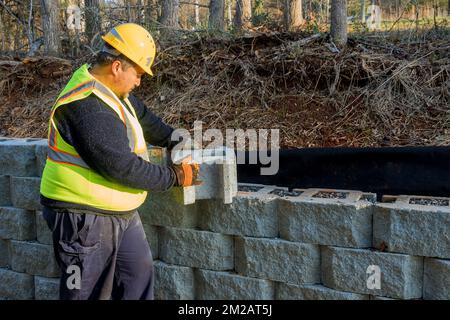 Mentre l'appaltatore stava installando la parete di ritegno di blocco grande di nuova costruzione nel cantiere Foto Stock