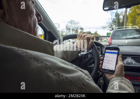 Uomo anziano irresponsabile al volante controllo messaggi su smartphone / smartphone / cellulare durante la guida di auto su strada | Homme agé derrière volant lisant messages sur smartphone / téléphone mobile en roulant en voiture 17/11/2017 Foto Stock