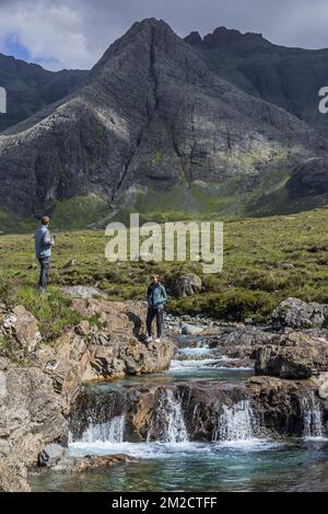 Black Cuillin e turisti che visitano le piscine delle fate, successione di cascate in Glen fragle sull'isola di Skye, Highlands scozzesi, Scozia, UK | Promeneurs visitent Fairy Pools à Glen fragle, île de Skye, Ecosse, Royaume-uni 02/06/2017 Foto Stock