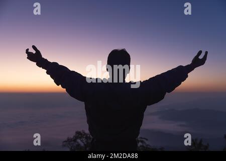 Silhouette di un giovane che prega Dio sulla montagna sullo sfondo del tramonto. alzando le mani nel culto. Concetto di religione cristiana. Foto Stock