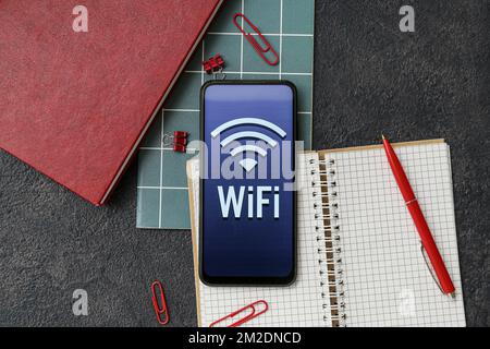 Articoli di cancelleria e telefono cellulare con simbolo WiFi su sfondo scuro, primo piano Foto Stock