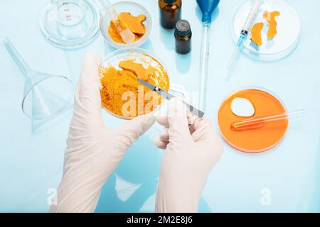 Ricerca medica delle proprietà curcuma con l'aiuto di attrezzature di laboratorio, donna in guanti di prova curcuma polvere. Vista dall'alto. Foto Stock