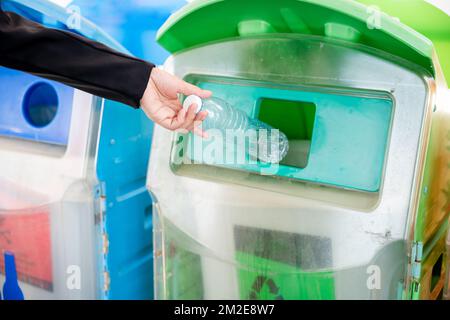 Donna d'affari che getta acqua vuota della bottiglia di plastica nei rifiuti di rifiuti di riciclaggio Foto Stock