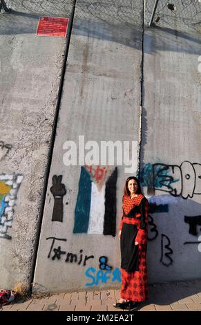 Una donna Palestinese in piedi dalla barriera costruita dal governo israeliano. La parete è dipinta con la bandiera palestinese. Foto Stock