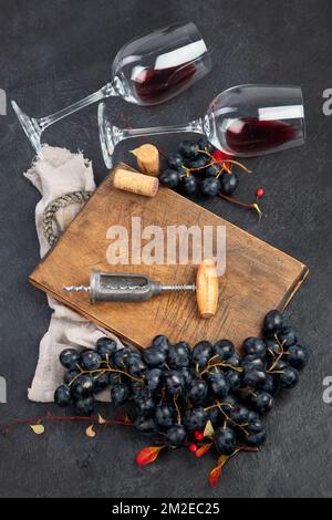 Una foto dall'alto di bicchieri di vino rosso con una bottiglia, uva, un corkscew e tappi d'annata, girati dall'alto su uno sfondo scuro. Vista dall'alto. Foto Stock