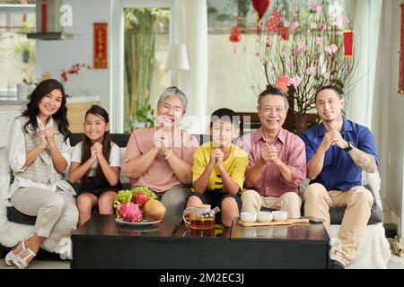 Smilng famiglia fare un gesto di saluto e guardare la fotocamera quando festeggia Tet a casa Foto Stock