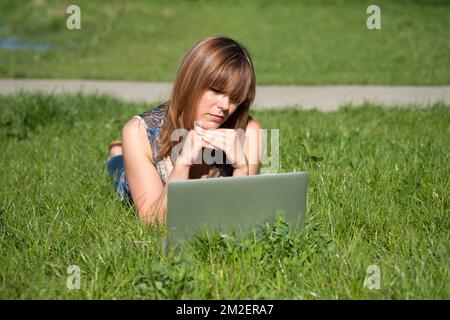 Giovane donna con un computer. | Jeune femme coouchée dans l'herbe avec un ordinateur. 05/05/2016 Foto Stock