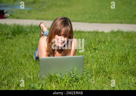 Giovane donna con un computer. | Jeune femme coouchée dans l'herbe avec un ordinateur. 05/05/2016 Foto Stock