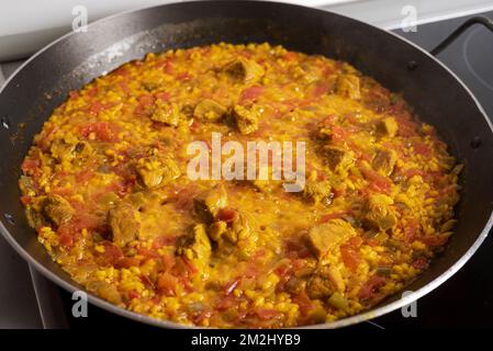 Padella con una paella di carne che sta per essere rimossa dal fuoco. Foto Stock