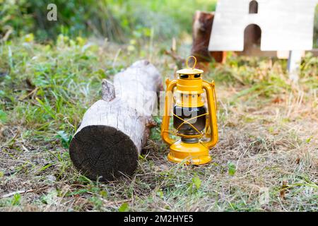 Sfocatura di una lampada a olio giallo vecchio stile su sfondo verde. Lampada kerosene. Cucinare, riscaldare un bollitore turistico su un bruciatore a gas portatile Foto Stock