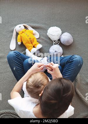 Madre insegnando figlia ragazza maglia giocattolo di pasqua coniglietto o coniglio. Vista dall'alto, fatta a mano e artigianato. La famiglia che crafting, spendendo il tempo nel paese Foto Stock