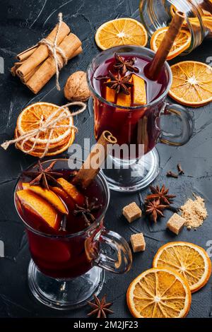 Due tazze di VIN brulé sulla tavola, vicino ad essa ci sono cannella, agrumi, arance secche, anice stellato, zucchero di canna. Produzione di VIN brulé a casa Foto Stock