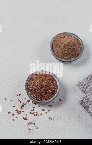 Semi di lino marroni e semi di lino macinati o frantumati in una piccola ciotola su sfondo grigio chiaro. Foto Stock