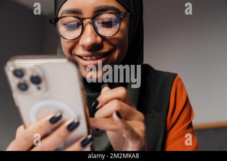 Young beautiful smiling woman in hijab and glasses with phone Foto Stock