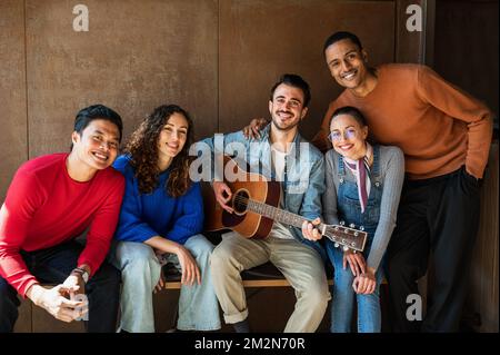 Gruppo multirazziale di giovani amici ritratto. Persone che guardano la telecamera con sorriso, si sta suonando la chitarra. Foto Stock