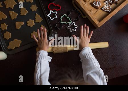 Una bambina tira fuori l'impasto con un matterello sul tavolo e prepara i biscotti di Natale Foto Stock