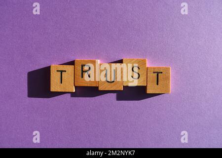 Fiducia, parola in lettere alfabetiche in legno isolato su sfondo viola Foto Stock