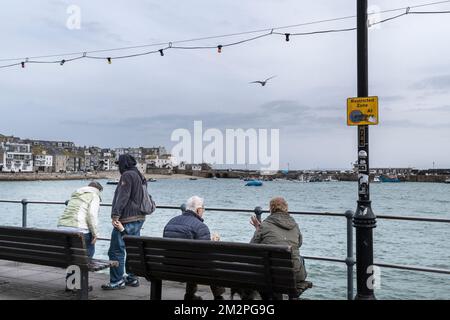 Meteo nel Regno Unito. I visitatori seduti su una panchina che si affaccia sul porto fino al Molo di Smeatons in una giornata piovosa e fredda nella storica cittadina costiera di Foto Stock