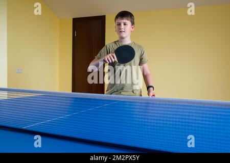 Un adolescente di 11 anni con una racchetta da tennis in mano sta giocando a Ping Pong. Stile di vita sportivo Foto Stock