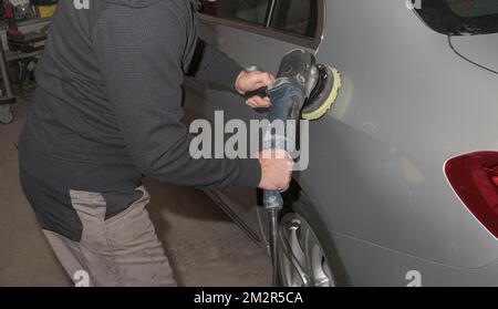 Lucidatura per auto. Addetto al servizio auto con lucidatore elettrico lucidante cappa d'argento in officina di riparazione auto Foto Stock