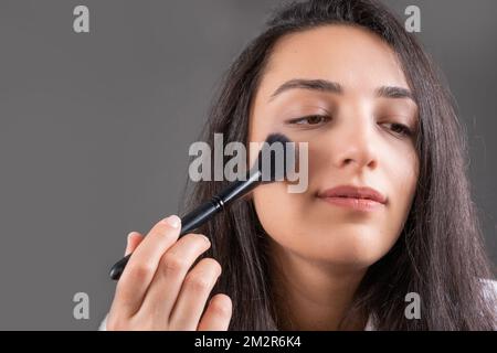 Applicare arrossamento, giovane ragazza caucasica. Polveri per il viso, utilizzando un pennello per fondazioni beige a zigomi. Idea di trucco perfetta e bella sensazione. Foto Stock