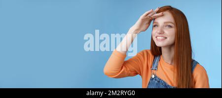 Ragazza guardare lontano distanza girare a sinistra tenere mano fronte di copertura gli occhi caldi luce del sole che sorridevano deliziati a guardare erano palla caduta peer afar gioiosamente squinting ottenere Foto Stock