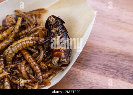 Grubs di legno fritti, lombrichi e scarafaggi su un tagliere di legno. Insetti fritti come fonte di proteine nella dieta. Foto Stock