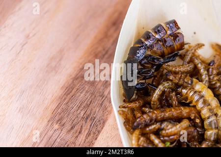 Grubs di legno fritti, lombrichi e scarafaggi su un tagliere di legno. Insetti fritti come fonte di proteine nella dieta. Foto Stock