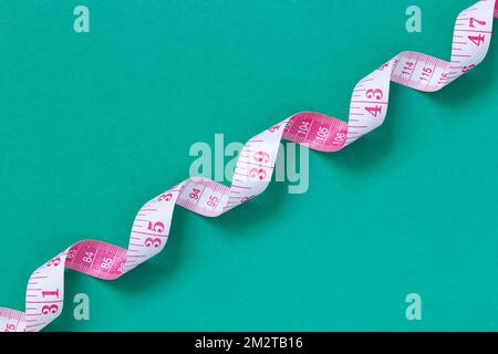 Nastro graduato bianco e rosa con marcature metriche e inch, avvolto a spirale su sfondo verde Foto Stock