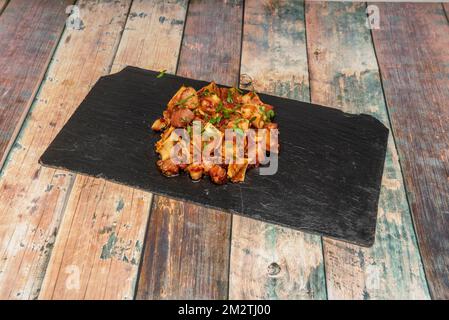 Una tipica tapa da bar spagnola con orecchie grigliate con salsa su un piatto di ardesia nera con prezzemolo fresco su un tavolo di legno Foto Stock