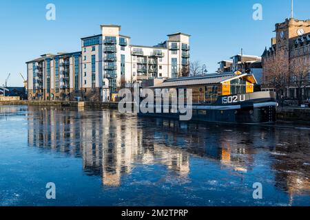 Leith, Edimburgo, Scozia, Regno Unito, 14th dicembre 2022. UK Weather: Water of Leith River Frozen: Le persistenti condizioni di congelamento hanno fatto congelare il fiume sulla riva creando colorati riflessi degli edifici e una casa galleggiante ormeggiata nel ghiaccio. Credit: Sally Anderson/Alamy Live News Foto Stock