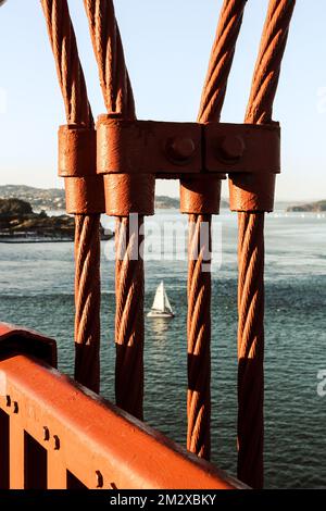 Immagine di una barca a vela sulla baia di San Francisco, ripresa dal Golden Gate Bridge, attraverso i suoi famosi cavi rossi Foto Stock