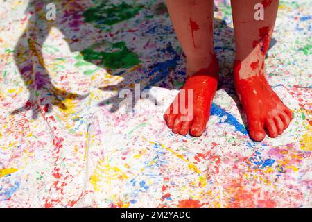 Primo piano del bambino utilizzando i piedi per dipingere alla luce del sole all'aperto con l'ombra delle mani in tiro Foto Stock