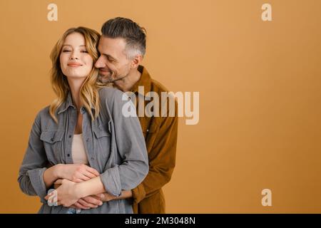 Bianco felice coppia indossando camicie sorridenti e abbraccianti isolato su sfondo beige Foto Stock