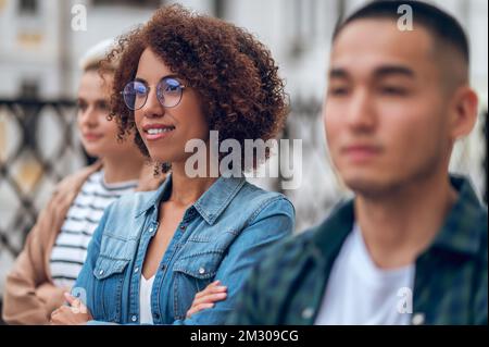 Donna allegra e bella e i suoi amici che guardano in lontananza Foto Stock